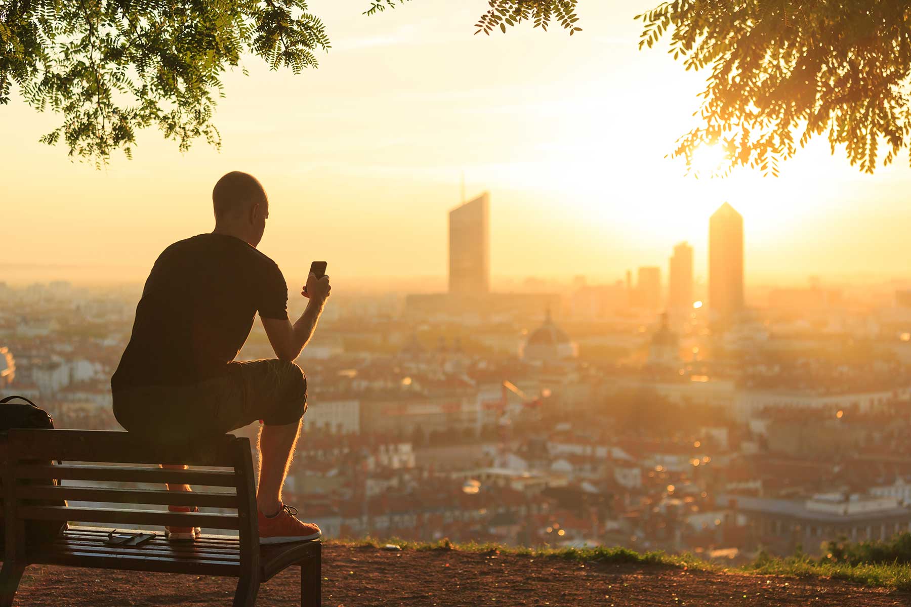 Person on phone enjoying beautiful view of the city and sunset while in one of the stages of recovery from substance use disorder