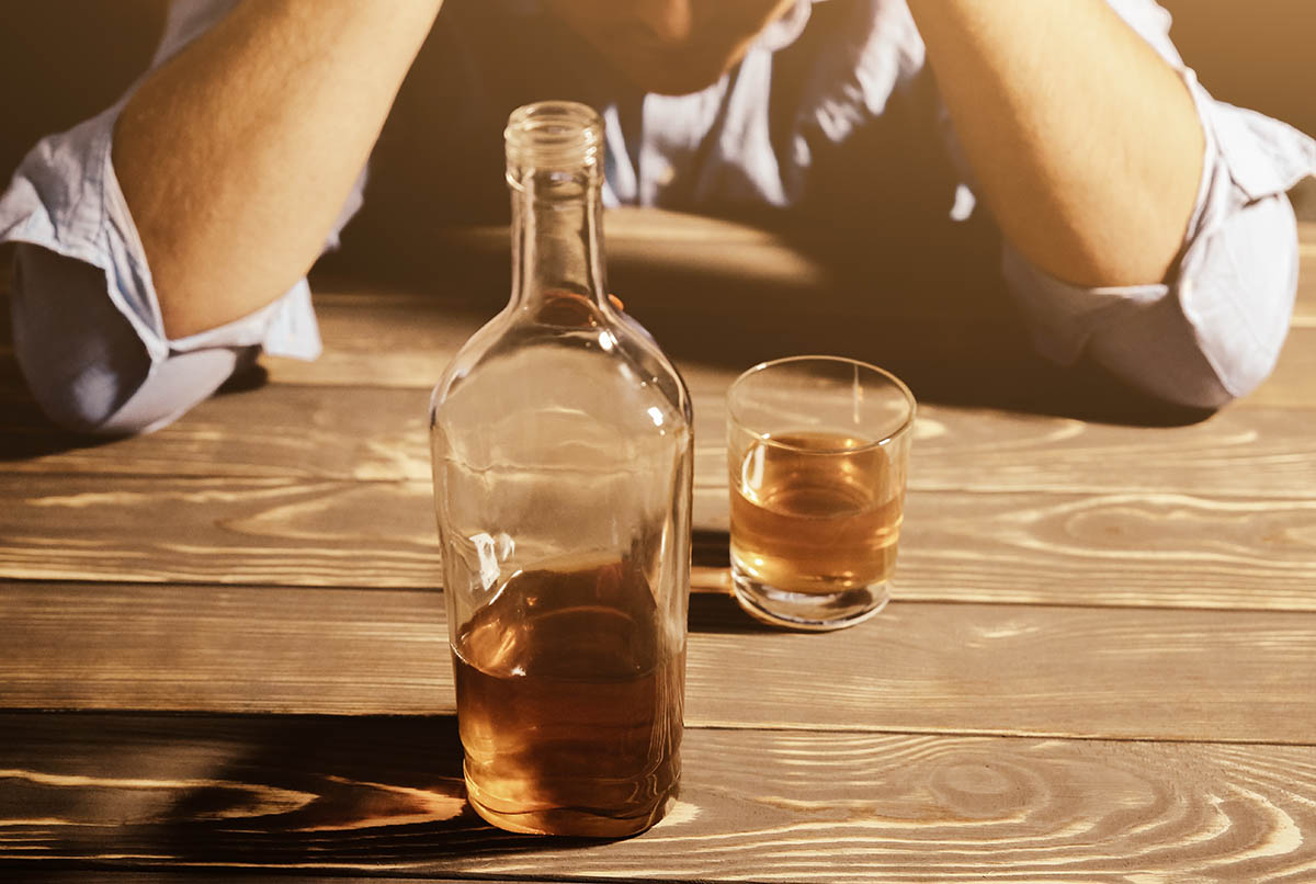 a man stares at a bottle and wonders about classifying alcohol as a drug