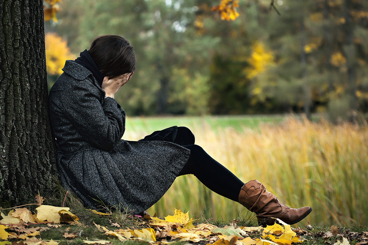 a woman leans against a tree and cries as she learns about the signs of heroin addiction