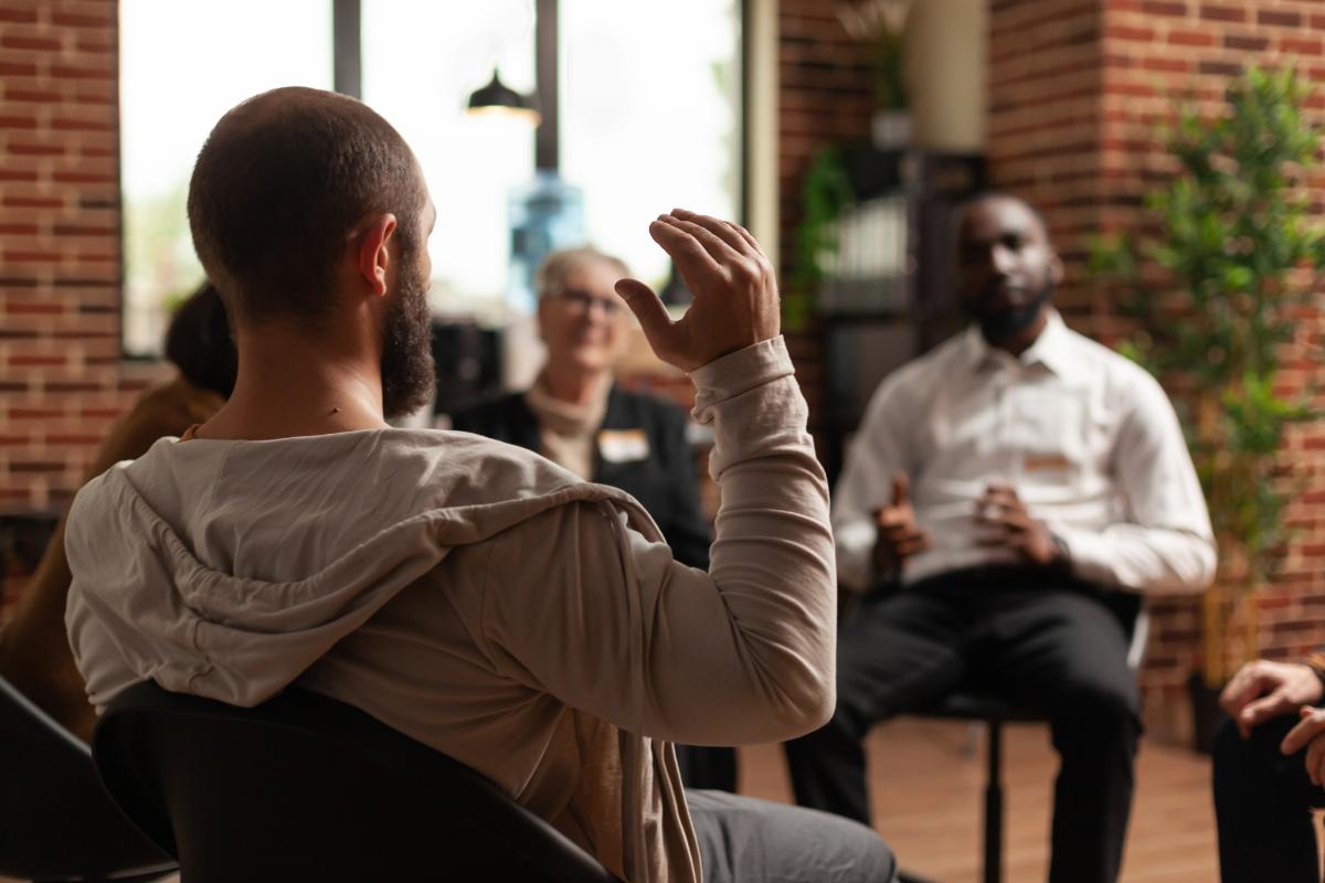 client raising hand in group therapy while learning about the benefits of dual diagnosis treatment