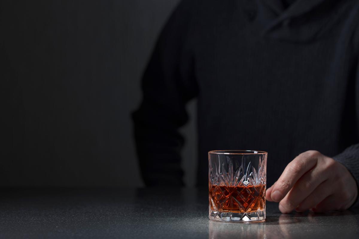 person's hand reaching for glass of liquor that may cause alcohol poisoning