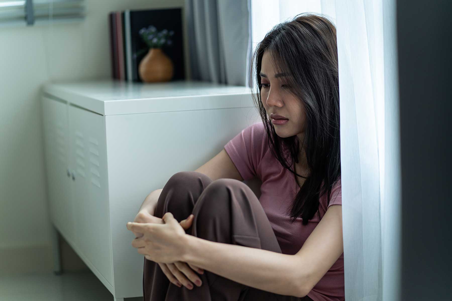Woman sitting on floor against a window struggling with depression and drug abuse